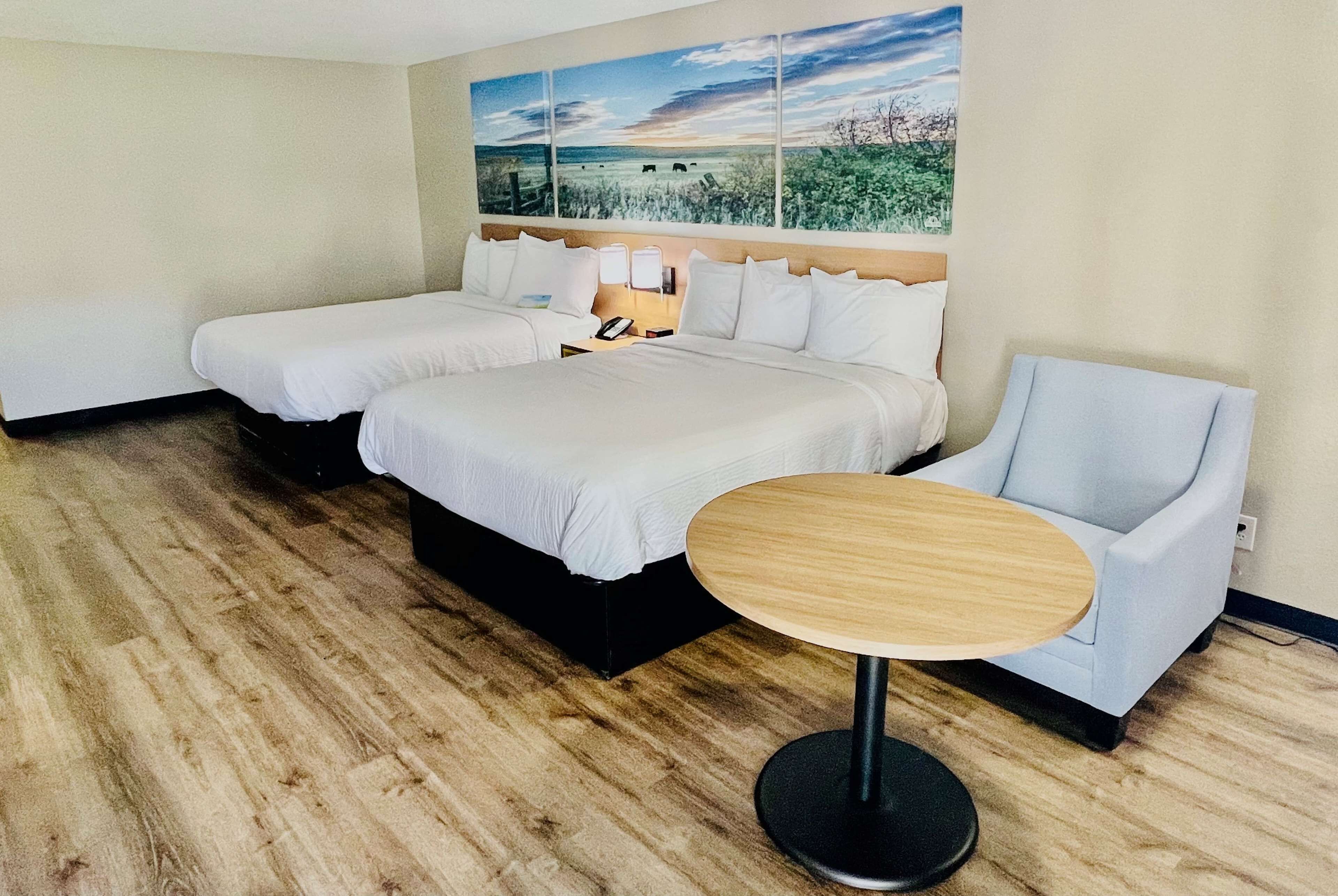 Quarto de hotel com duas camas, uma mesinha redonda e uma cadeira.