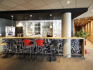 Un espace bar agrémenté d’un décor mural à motifs, de tabourets de bar et de luminaires suspendus.