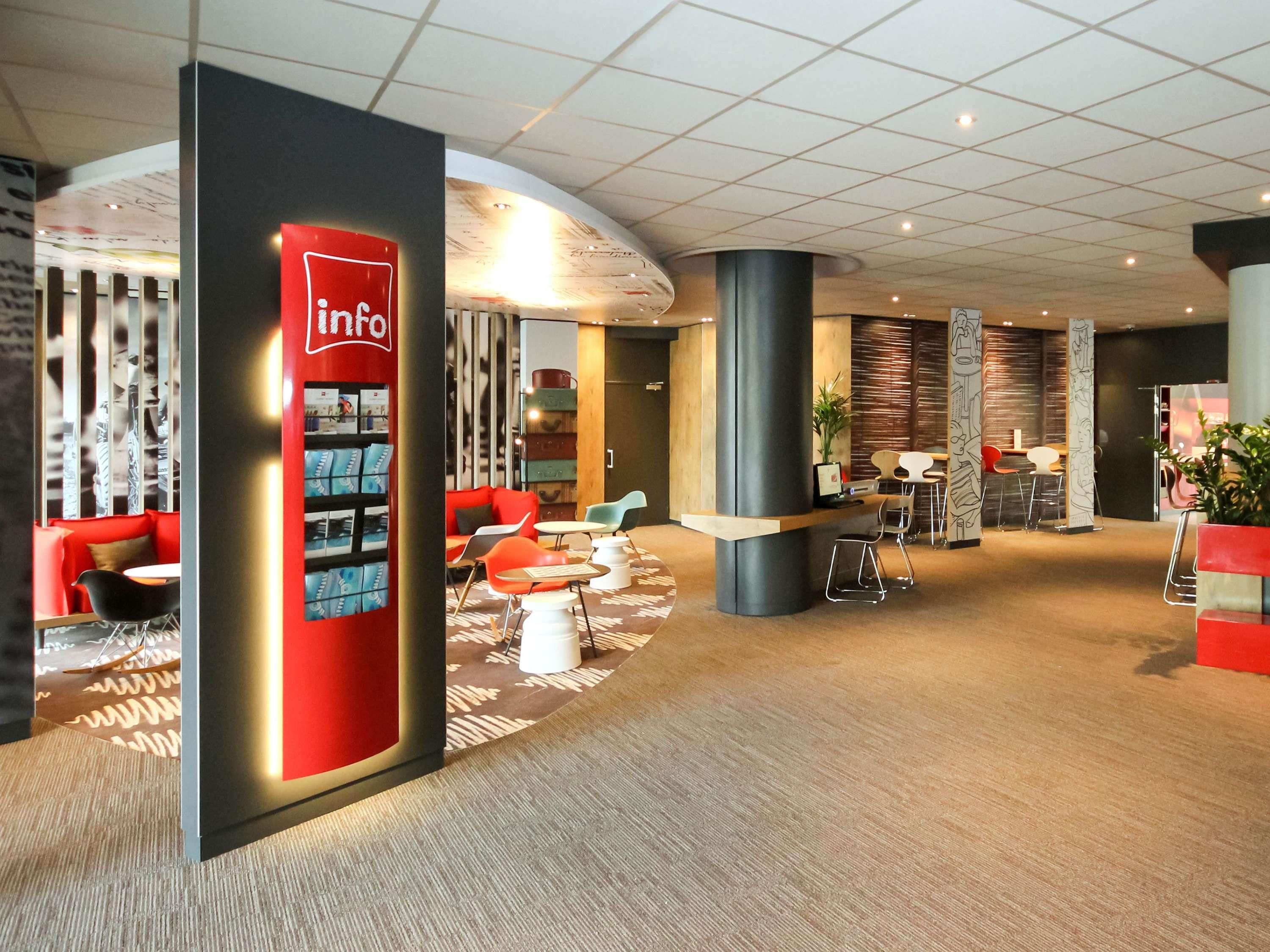 Un hall d’entrée moderne avec un comptoir d’information rouge, des espaces de détente et un tapis à motifs.