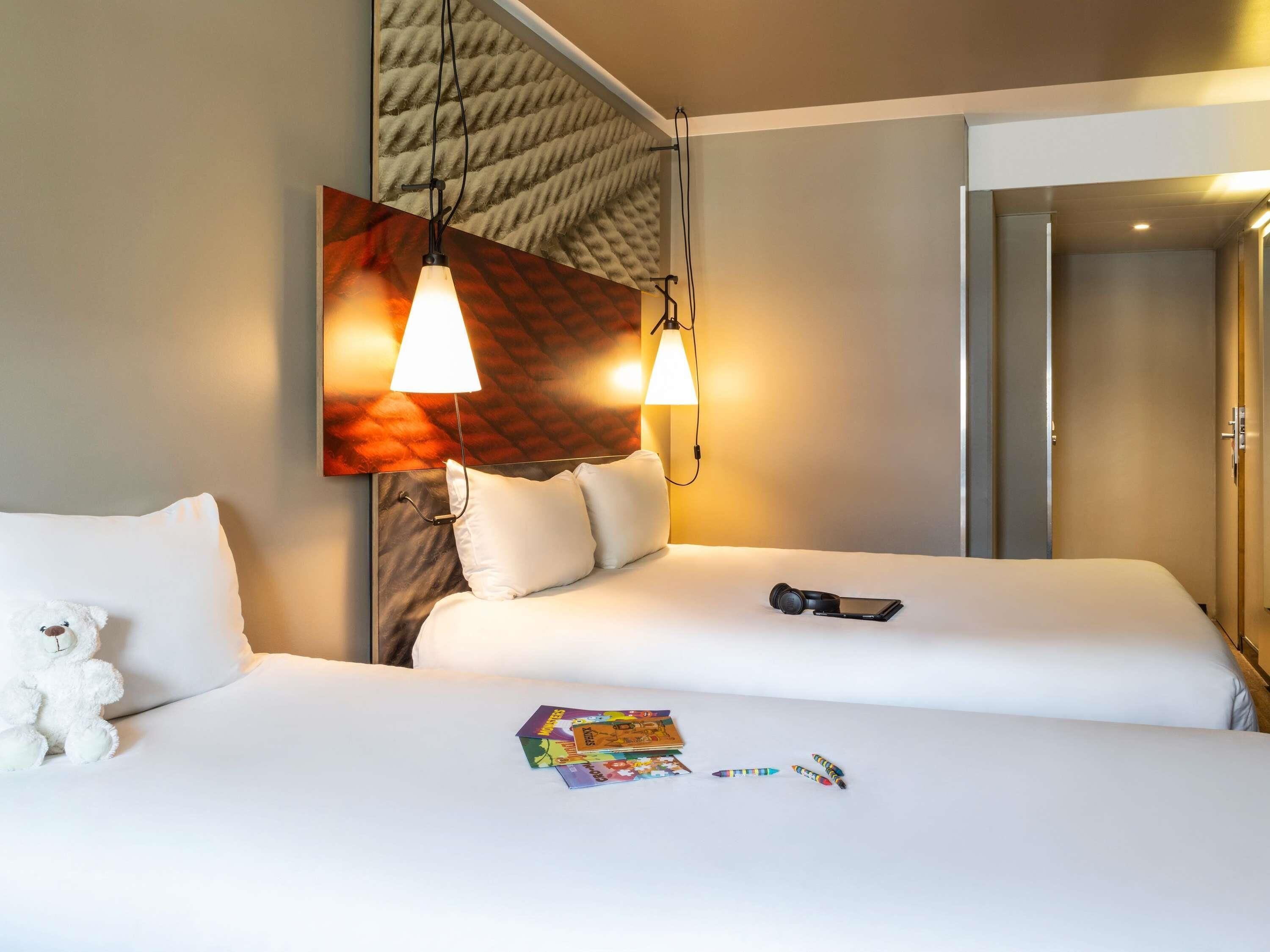 A hotel room with a bed, pillows, a stuffed toy, a smartphone, and a wall-mounted lamp.