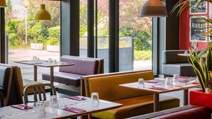 Een restaurant met grote ramen, tafels met stoelen en een rode accentmuur.