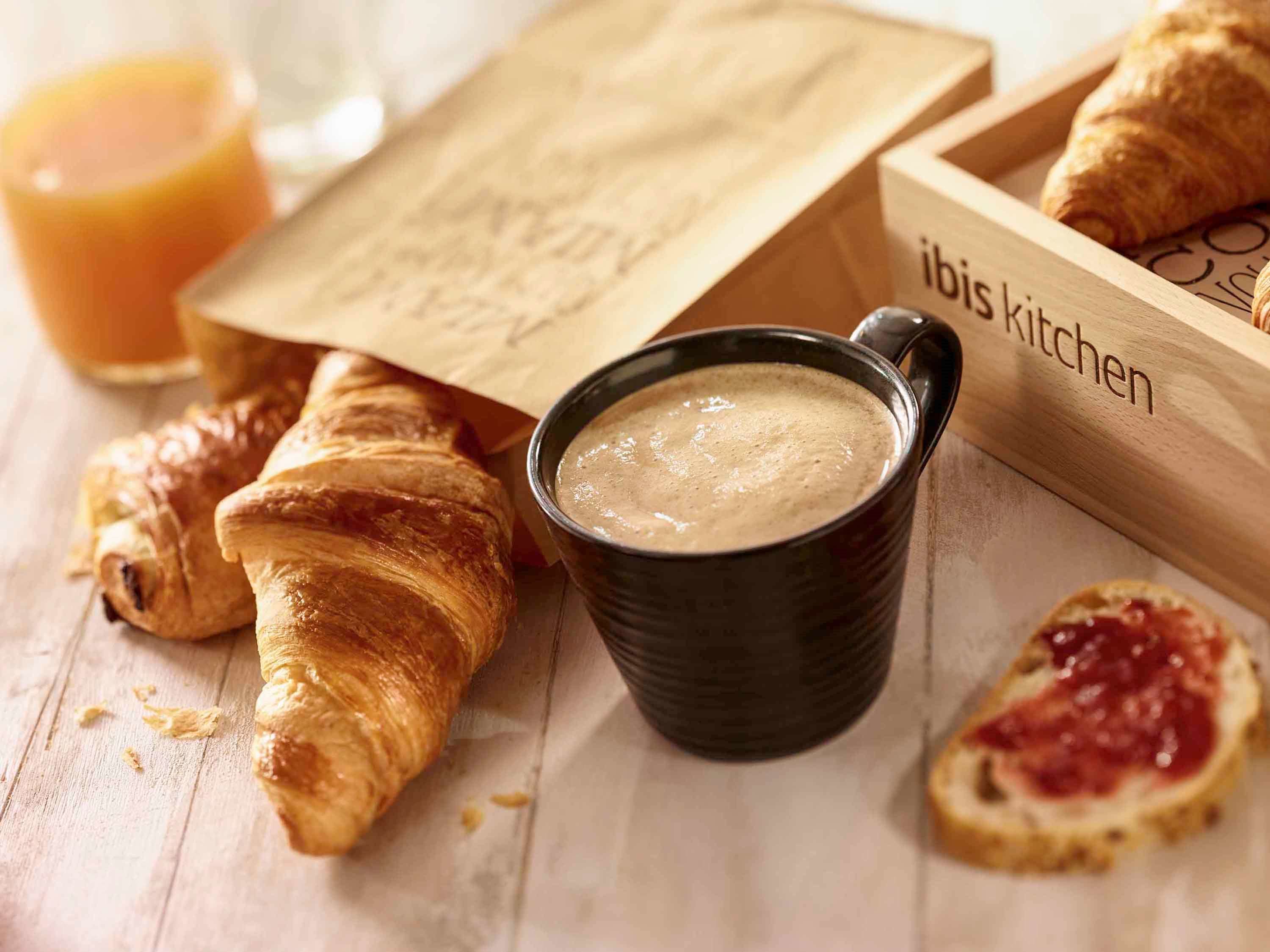 A wooden tray with croissants, a cup of coffee, and a glass of orange juice.