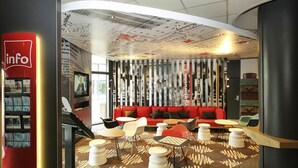 Een moderne lobby met een rode bank, witte en zwarte stoelen, een kamerbreed tapijt en een grote informatiezuil.