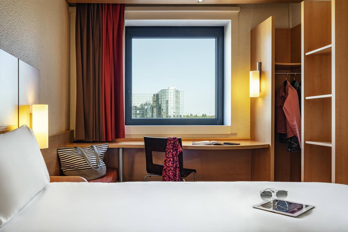 Habitación de hotel con cama, escritorio, silla, ventana con vista a edificios y armario.