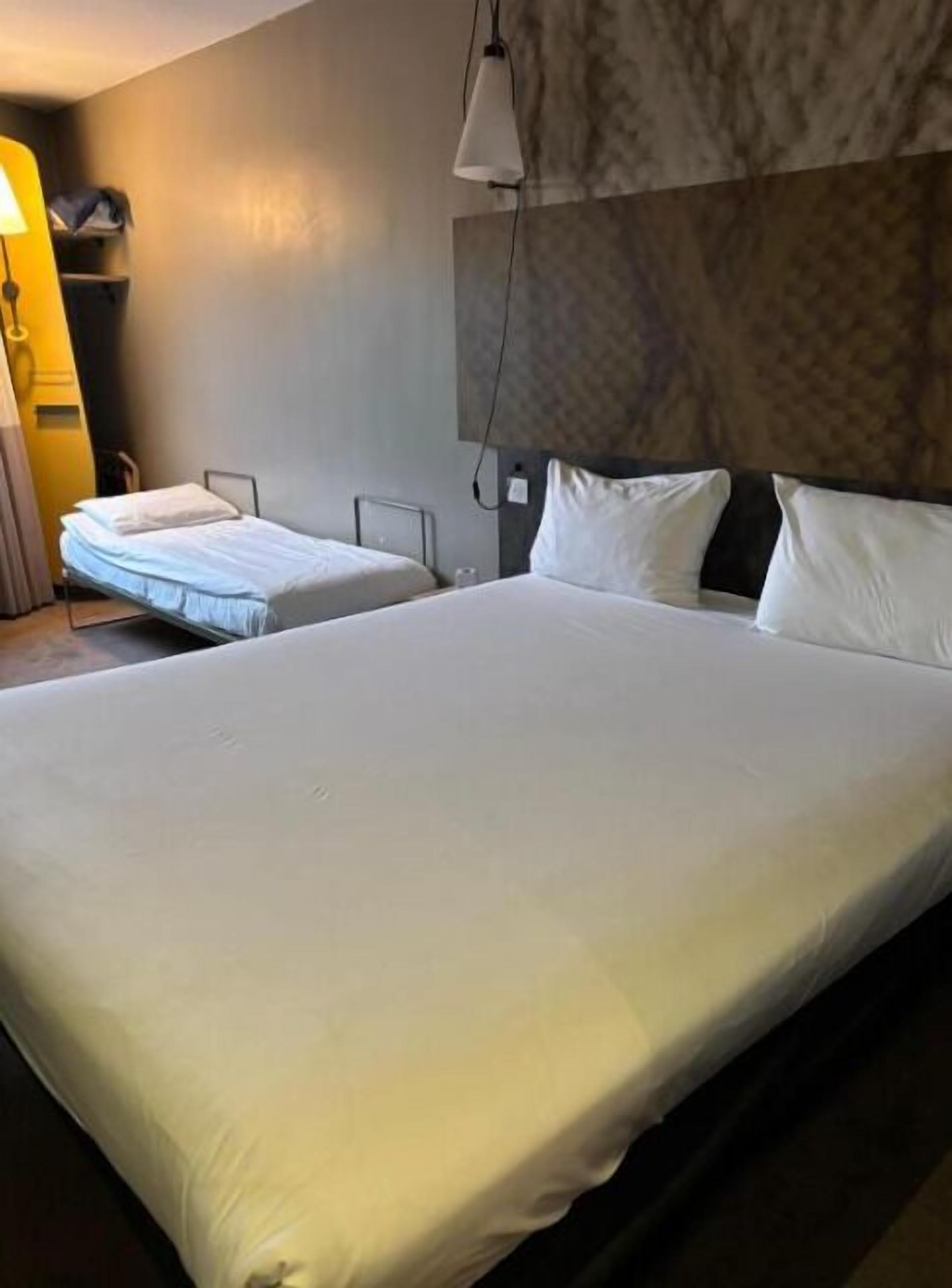 Una habitación de hotel con una cama grande, una cama más pequeña, un escritorio y una lámpara.