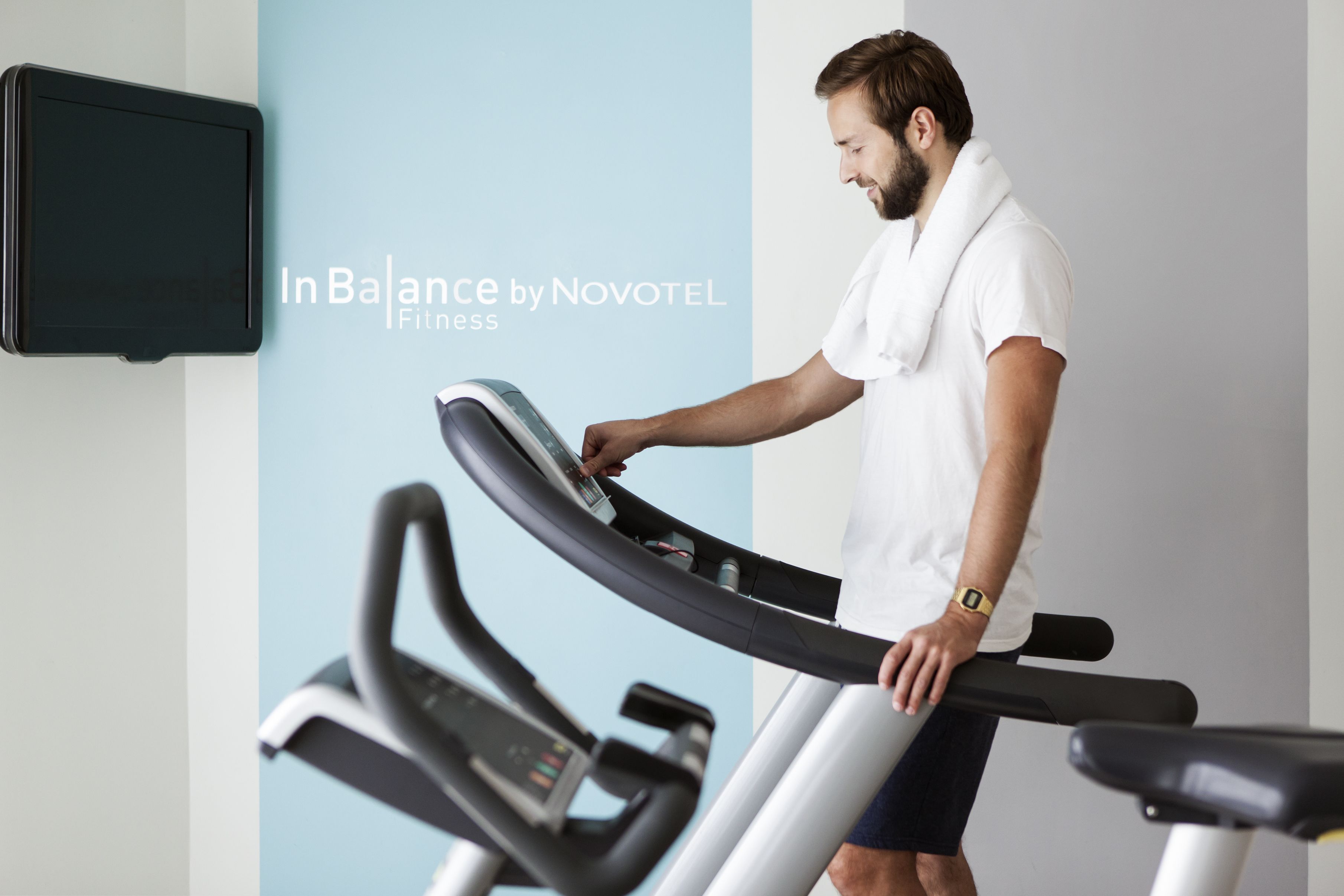 A man using a treadmill in a fitness area with a Novotel sign.