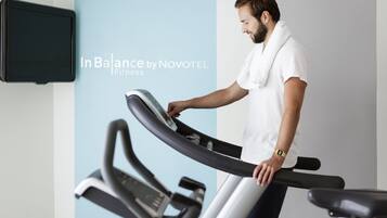 A man using a treadmill in a fitness area with a Novotel sign.