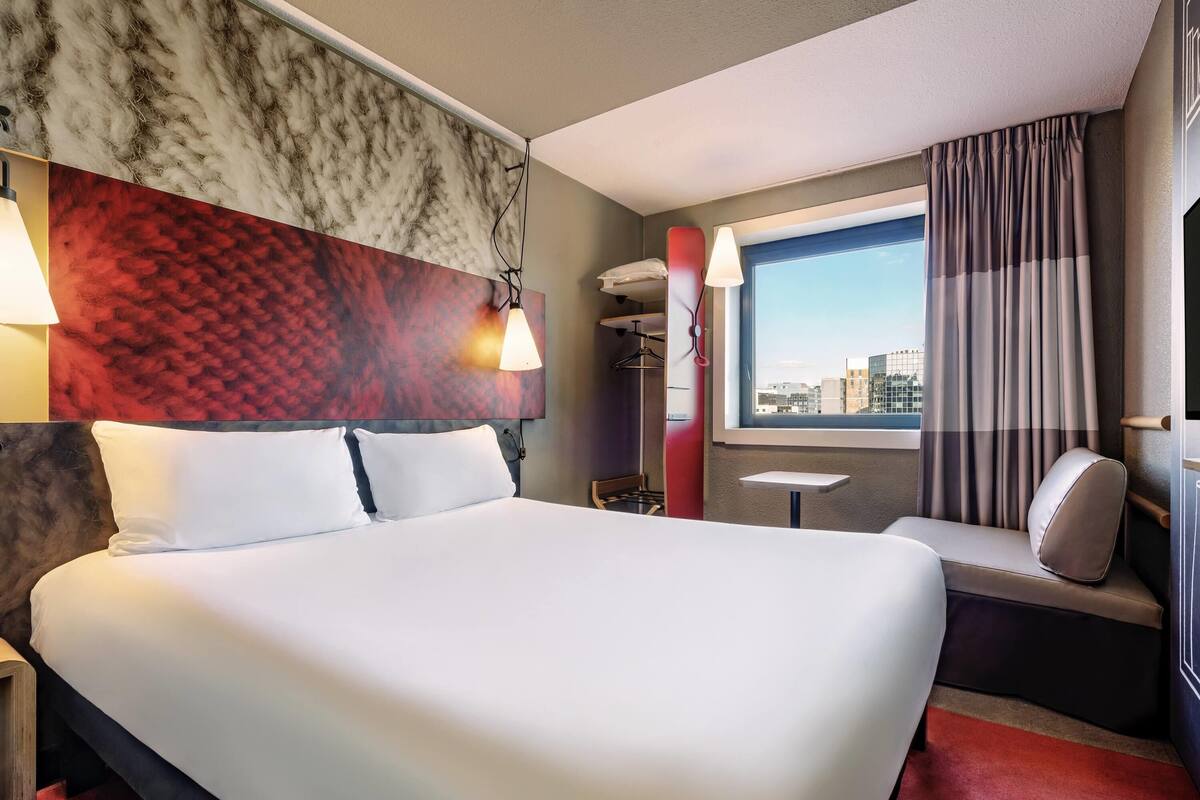 Een hotelkamer met een groot bed, een klein tafeltje, een bank en uitzicht op de stad, met gordijnen voor het raam.