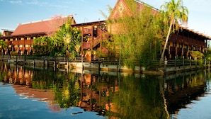 A building with a red roof, a balcony, and a reflection in the water. - Disney's Polynesian Village Resort (Lake Buena Vista)