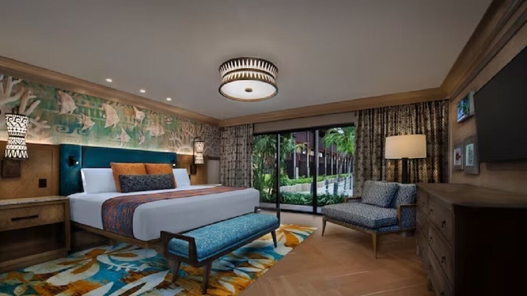 Hotelkamer met een bed, een bankje, een stoel, een dressoir, een lamp, een plafondlamp en uitzicht op groen.