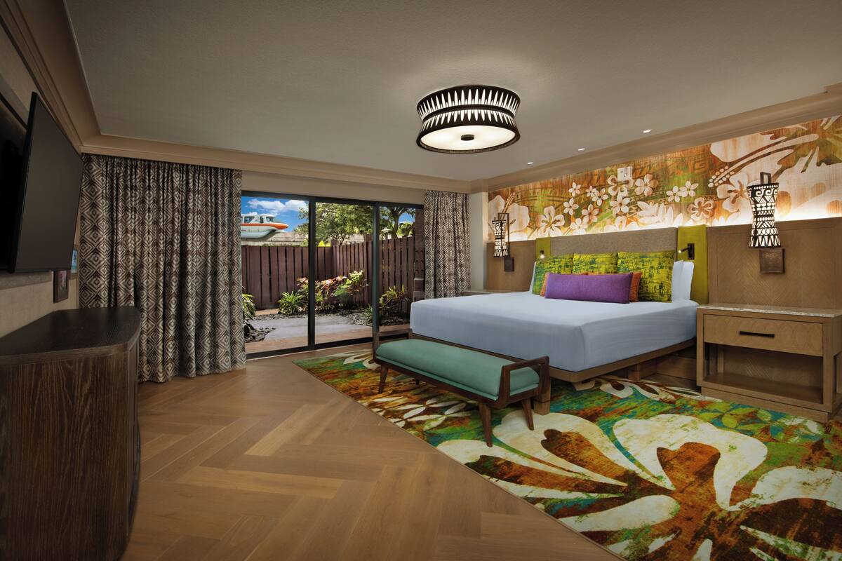 Un dormitorio moderno con una cama grande, un banco, una mesita de noche de madera y vistas al exterior.