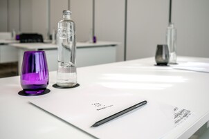 Ein weißer Tisch mit einem schwarzen Stift, einem violetten Glas und einer klaren Flasche.