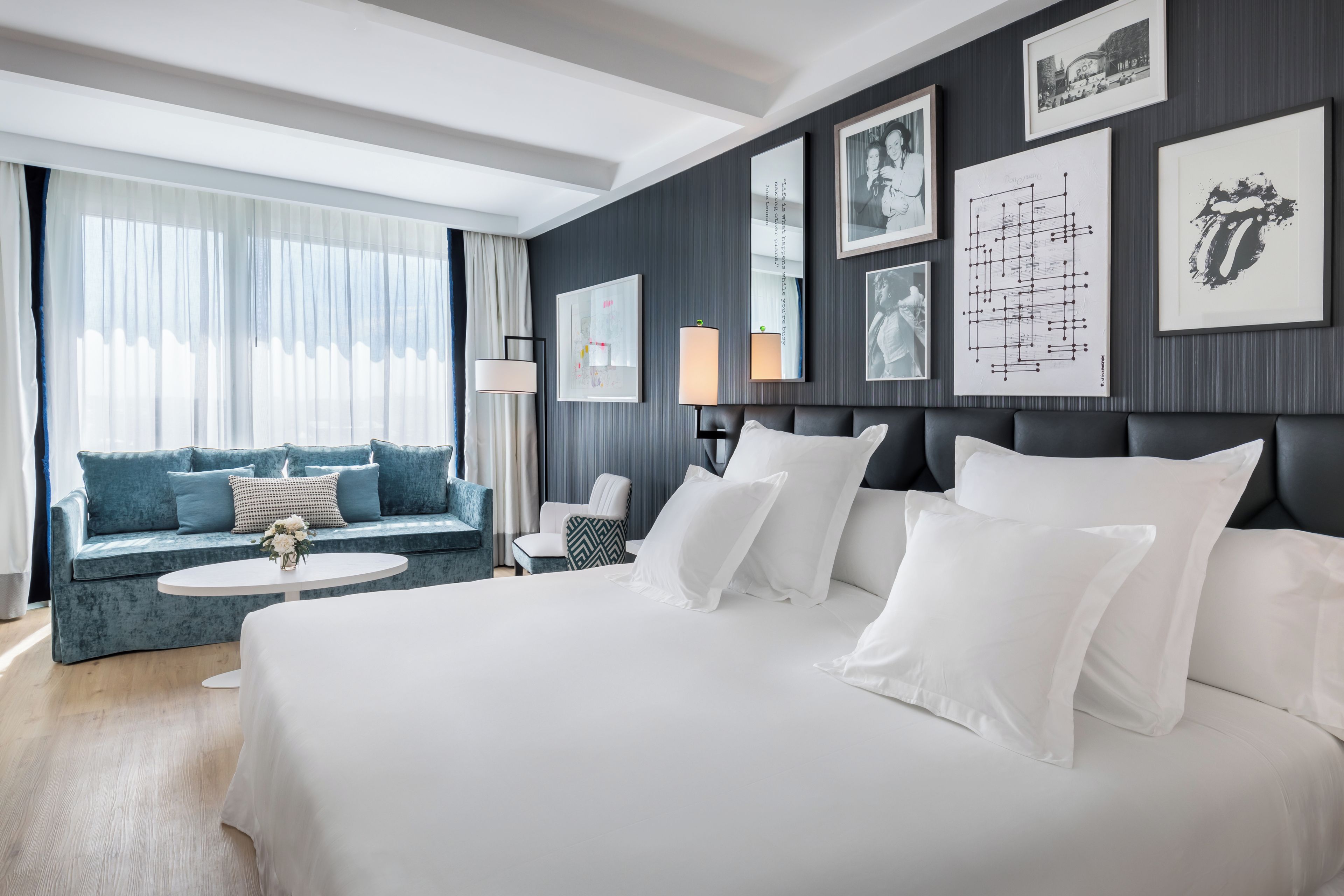 A hotel room with a large bed, a sofa, a small table, and a window with curtains.
