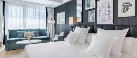 A hotel room with a large bed, a sofa, a small table, and a window with curtains.