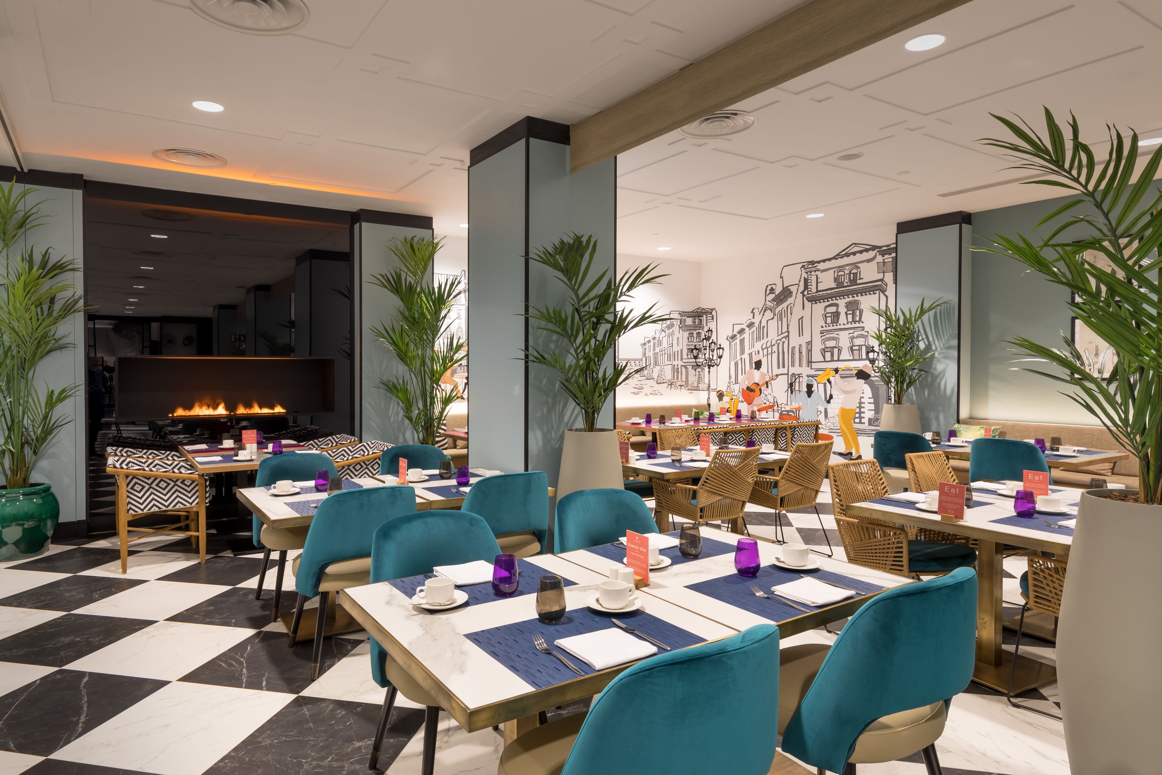 A modern restaurant with checkered flooring, teal chairs, and a fireplace.