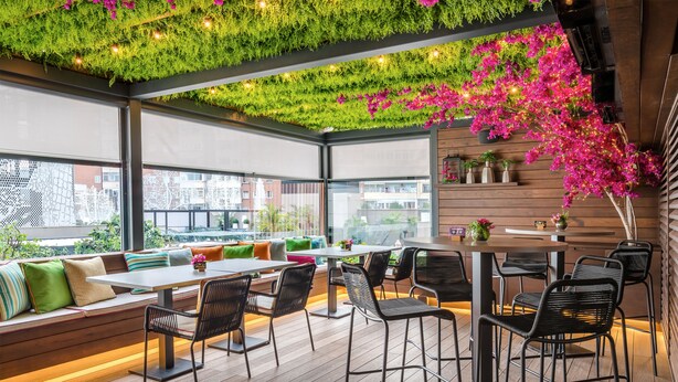A rooftop bar with wooden flooring, black metal chairs, and a seating area with cushions. - Barceló Imagine (Madrid)