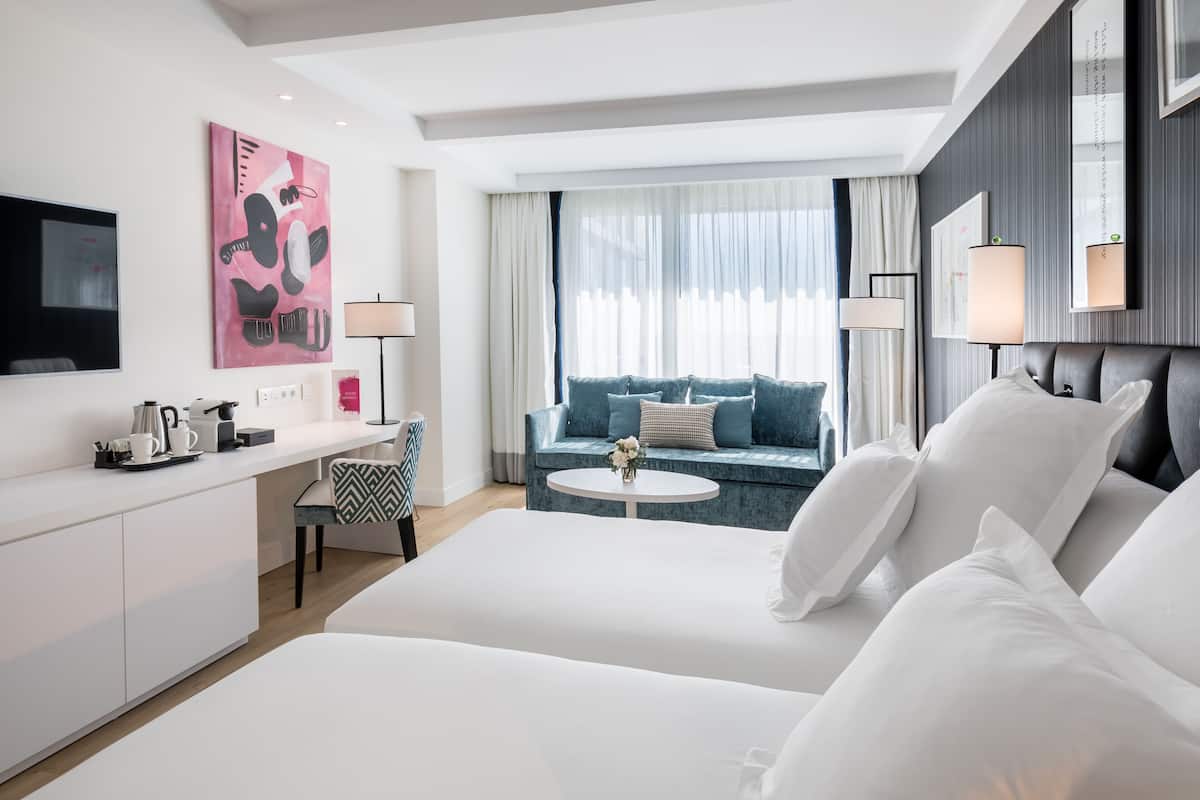 A modern hotel room with a large bed, a desk, a sofa, and a TV.