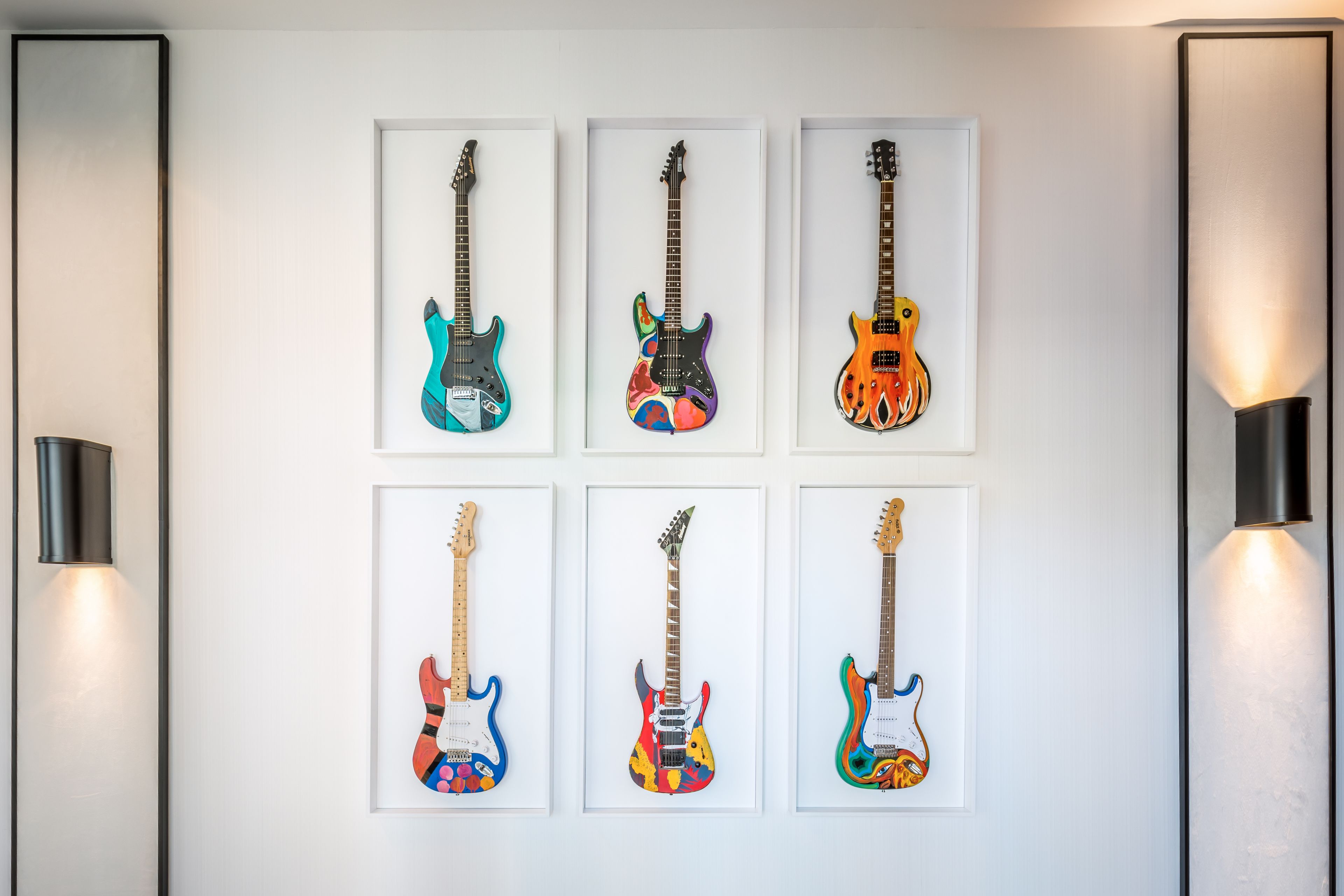 Seis guitarras eléctricas enmarcadas sobre una pared blanca, cada una con diseños únicos.