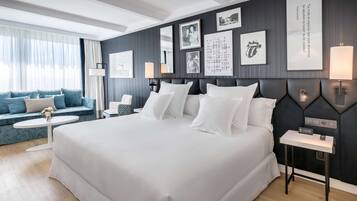 Una habitación de hotel moderna con una cama grande, un sofá, una mesita pequeña y una mesita de noche con una lámpara.