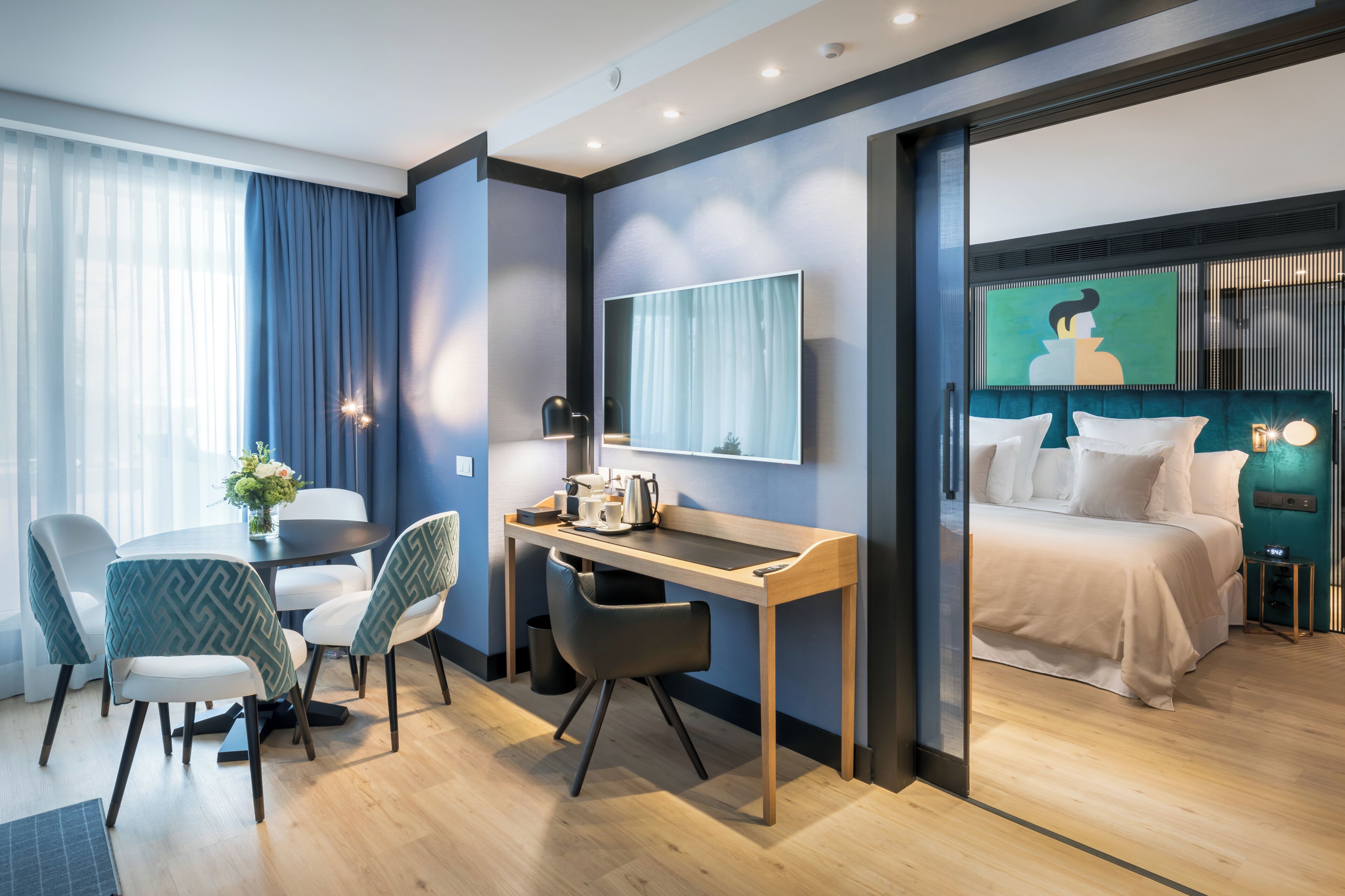 Habitación de hotel moderna con escritorio, sillas, cama, televisor y un cuadro en la pared.