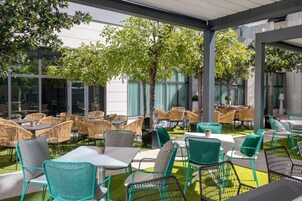 An outdoor patio area with multiple tables and chairs, surrounded by greenery and trees.