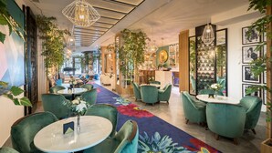 A modern interior with green upholstered chairs, a central floral carpet, and hanging pendant lights. - Barceló Imagine (Madrid)