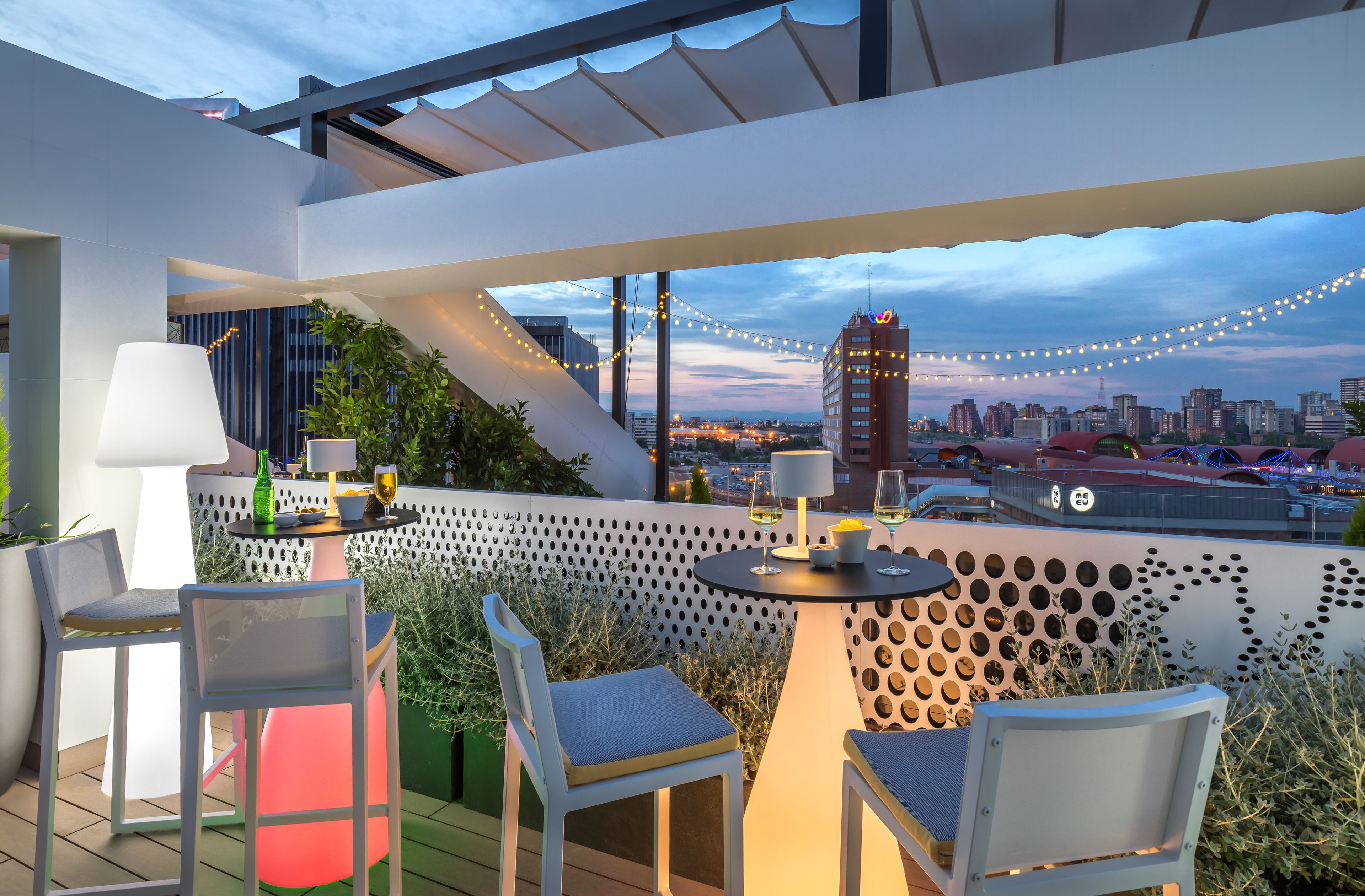 Una terraza en la azotea con mobiliario exterior, luces colgantes y vistas de la ciudad.
