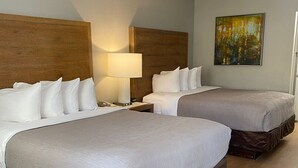 Hotellihuone, jossa on kaksi sänkyä, yöpöytä lampun kanssa ja taulu seinällä.