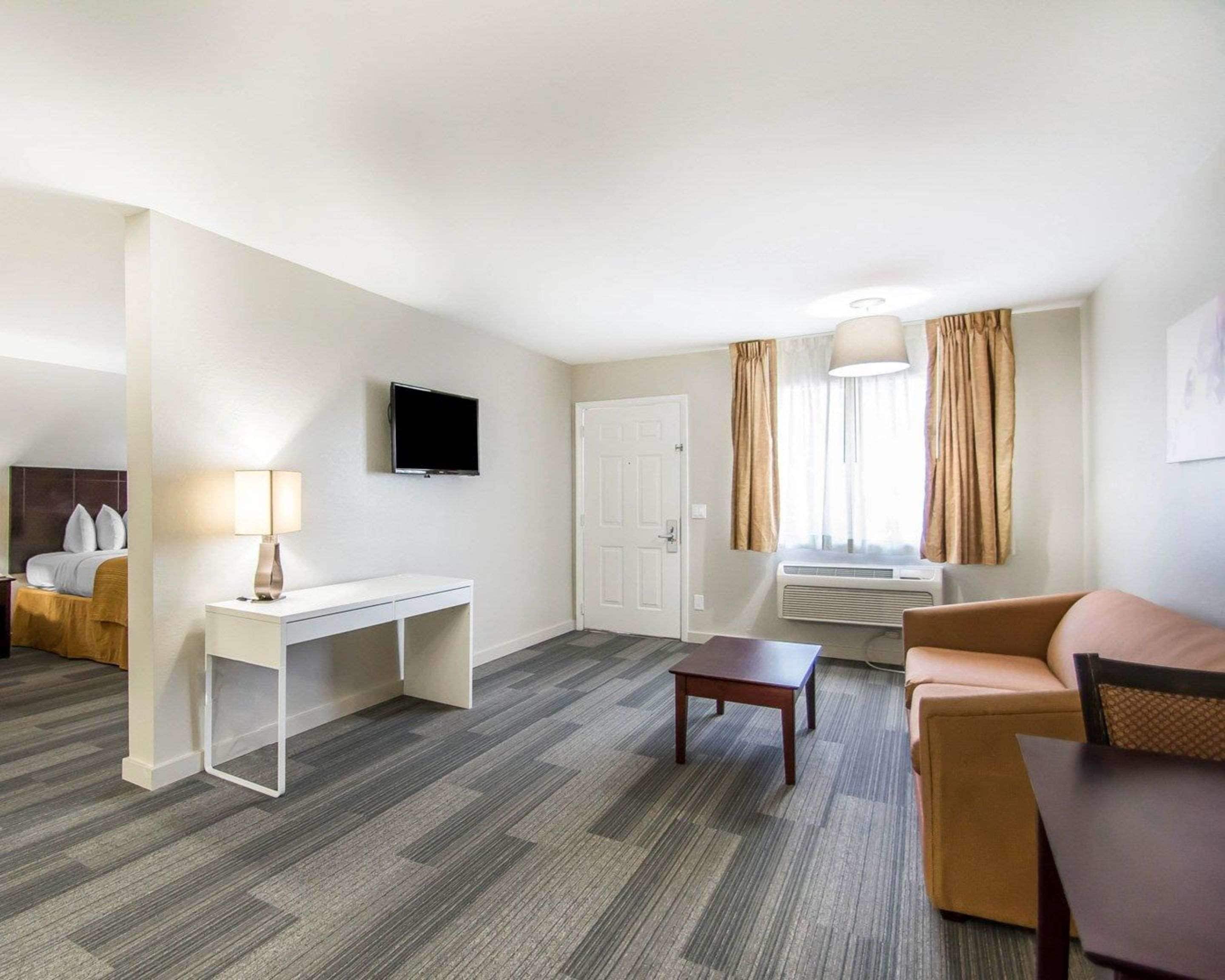 A hotel room with a bed, a desk, a television, a couch, and a window with curtains.