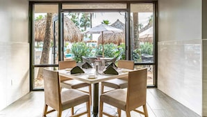 A dining area with a table set for four, large windows, and a view of an outdoor area with umbrellas and greenery. - Holiday Inn Resort Panama City Beach by IHG (Panama City Beach)