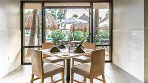 Comedor con mesa para cuatro, ventanas amplias y vista a un espacio exterior con sombrillas y follaje.