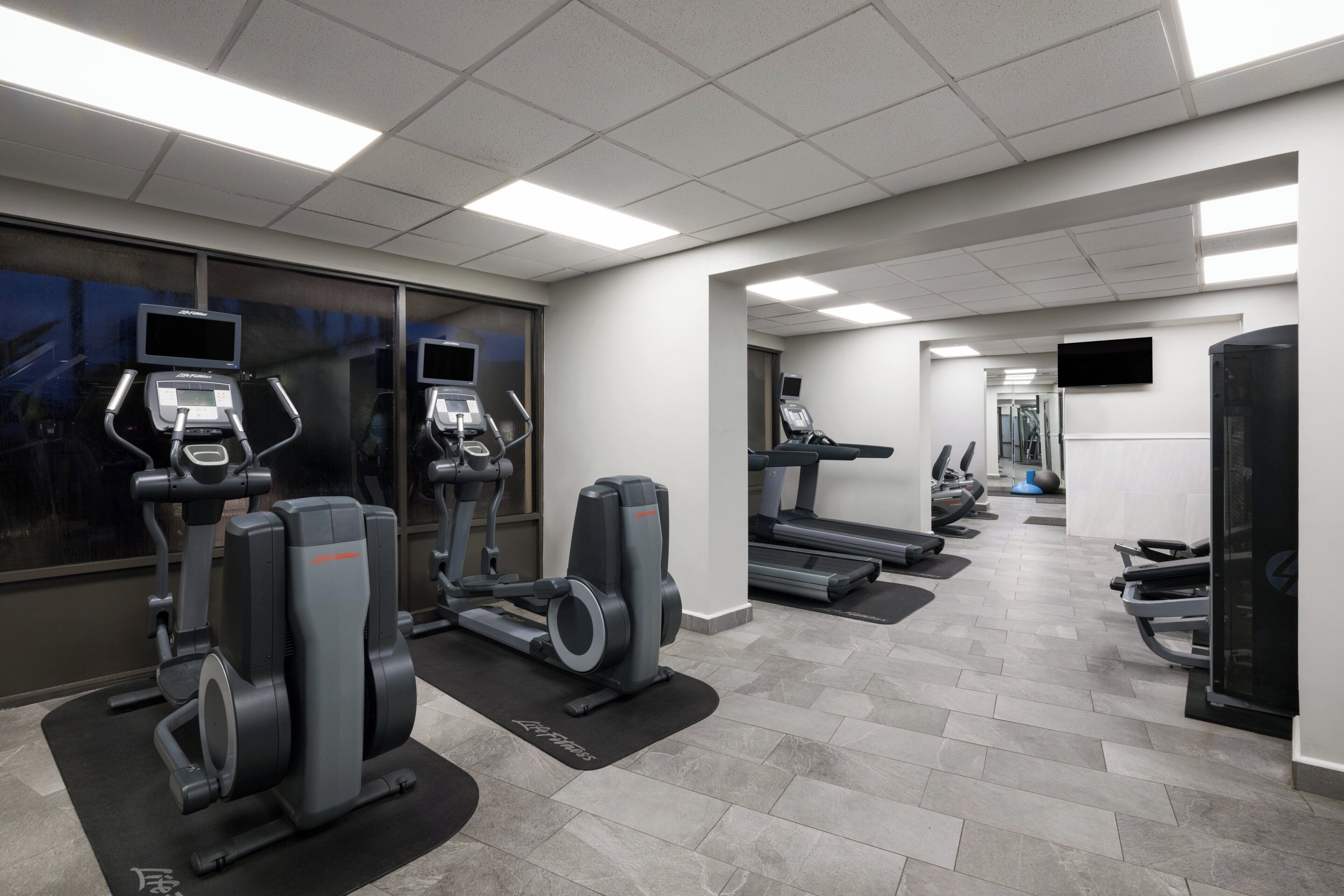 A gym with treadmills, elliptical machines, and a television screen.