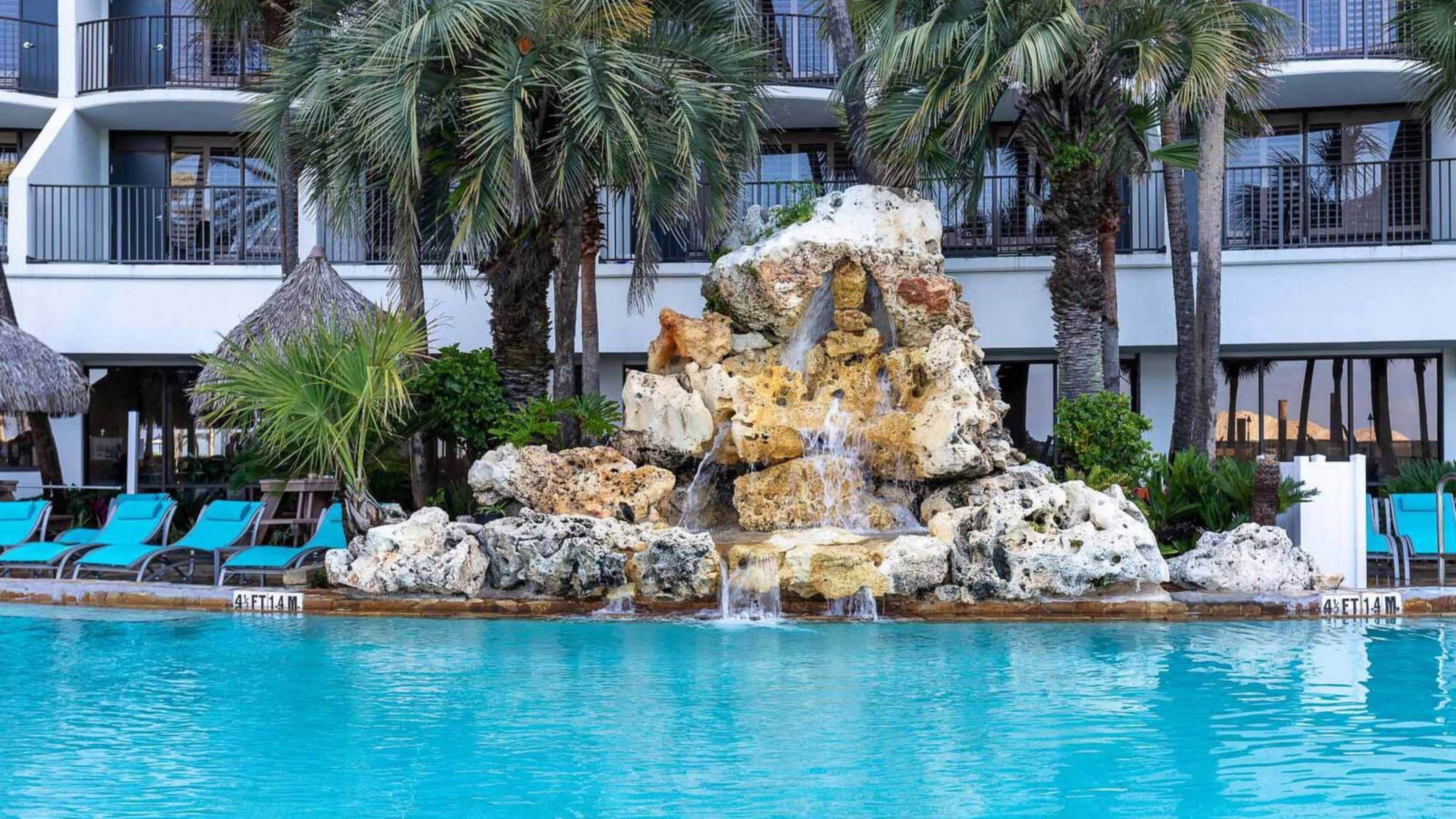 A pool with a rock waterfall, lounge chairs, and palm trees.