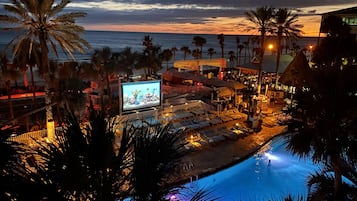 Un resort con piscina, lettini e un grande schermo che mostra una partita.