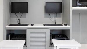 Estación de trabajo con dos monitores, dos teclados y dos ratones, un escritorio blanco y un armario cerrado con equipo electrónico.