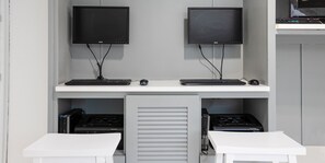 Estación de trabajo con dos monitores, dos teclados y dos ratones, un escritorio blanco y un armario cerrado con equipo electrónico.