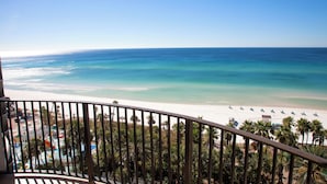 Un balcón con vista a una playa, palmeras y una zona de piscina.