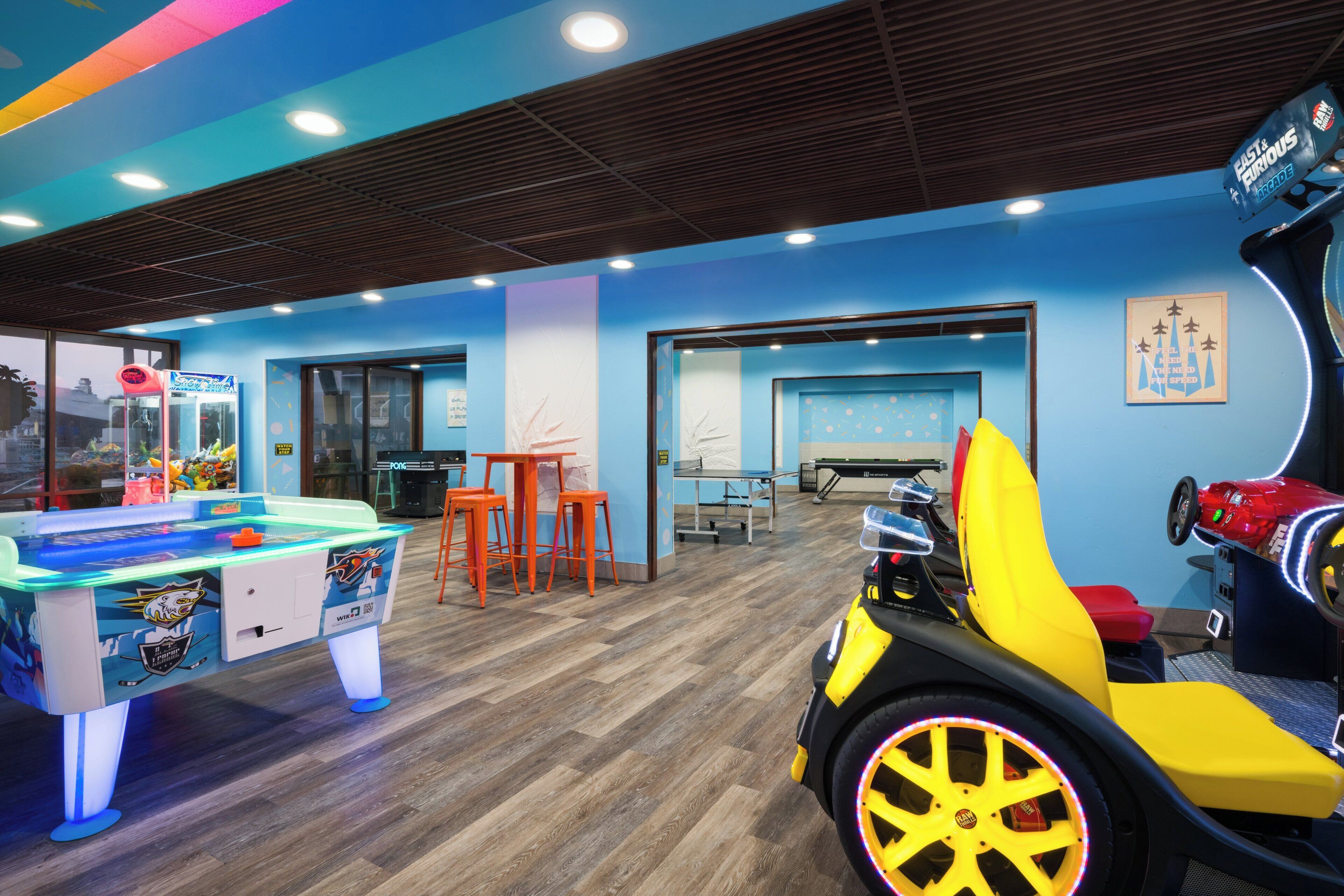 Un espace de jeux intérieur, bien éclairé, comprenant une table de billard, des jeux d’arcade et un parcours en petites voitures.