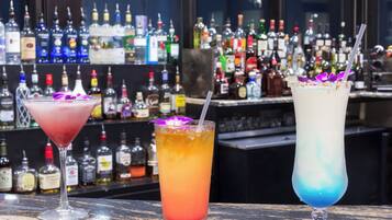 Three cocktails on a bar counter with a background of various liquor bottles.