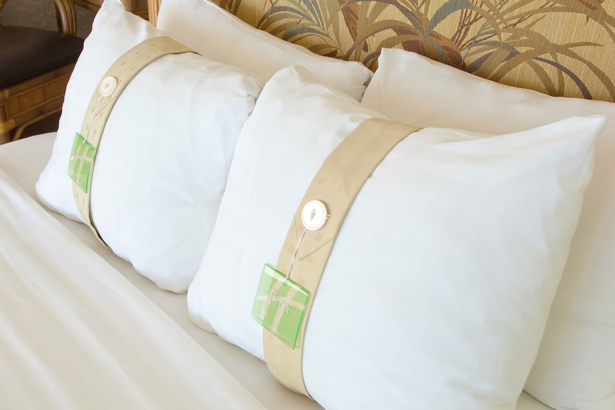 A bed with white bedding and three pillows with beige and green tags.
