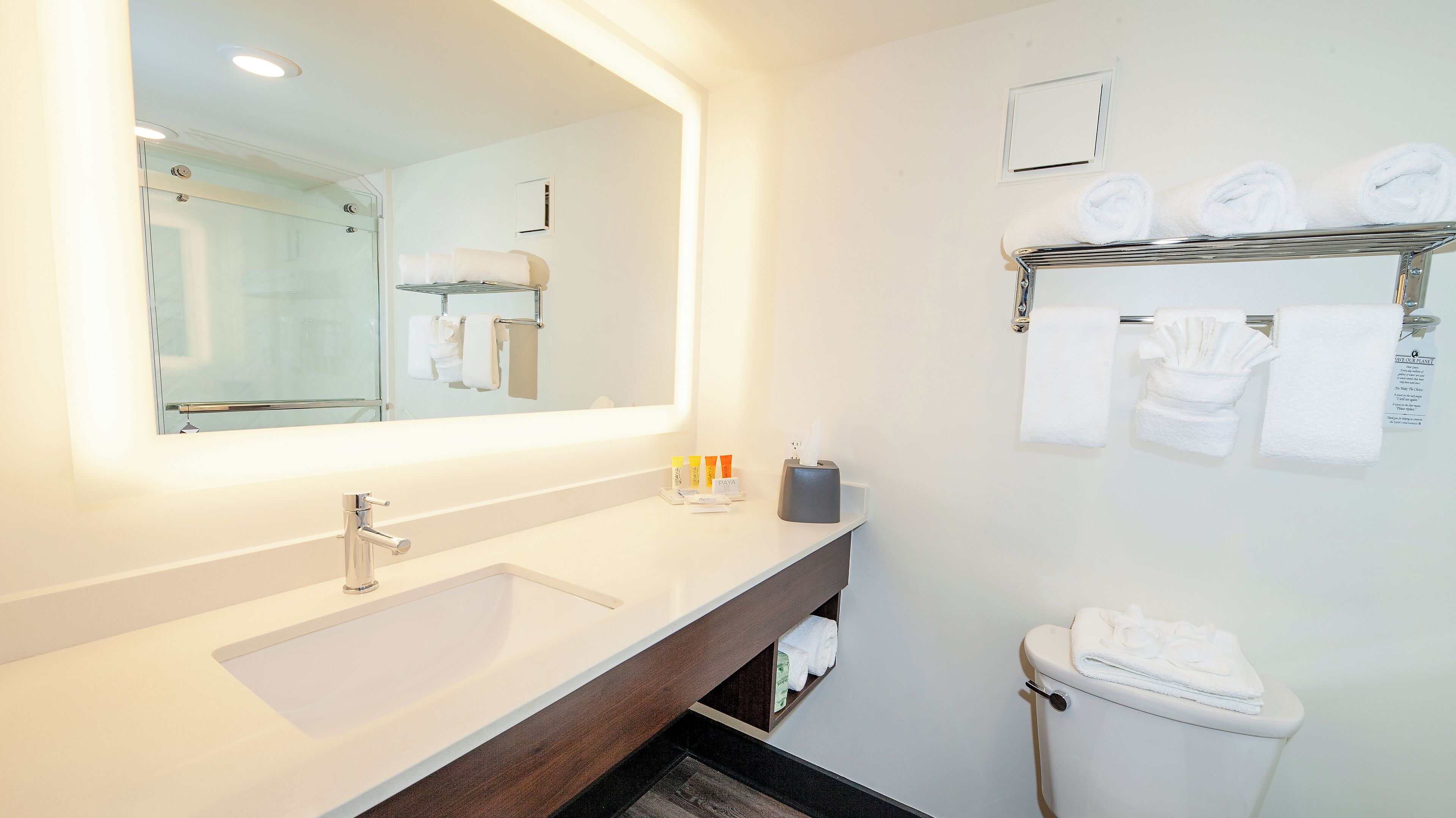 A modern bathroom with a large mirror, a sink, a toilet, and a towel rack.