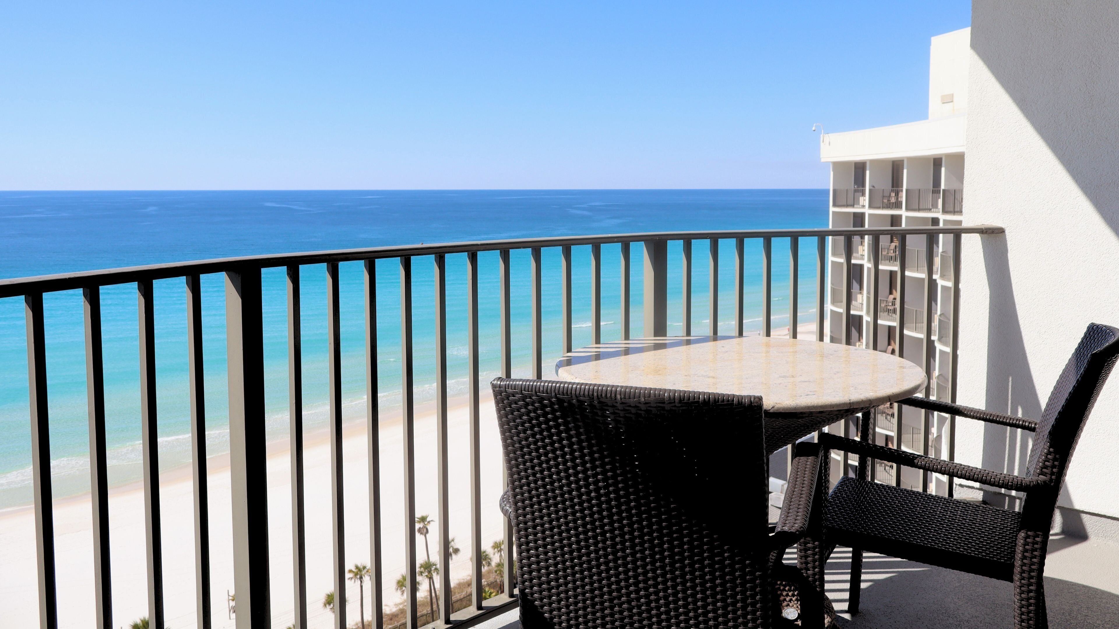 Un balcon avec une table et des chaises, donnant sur une plage et l’océan.