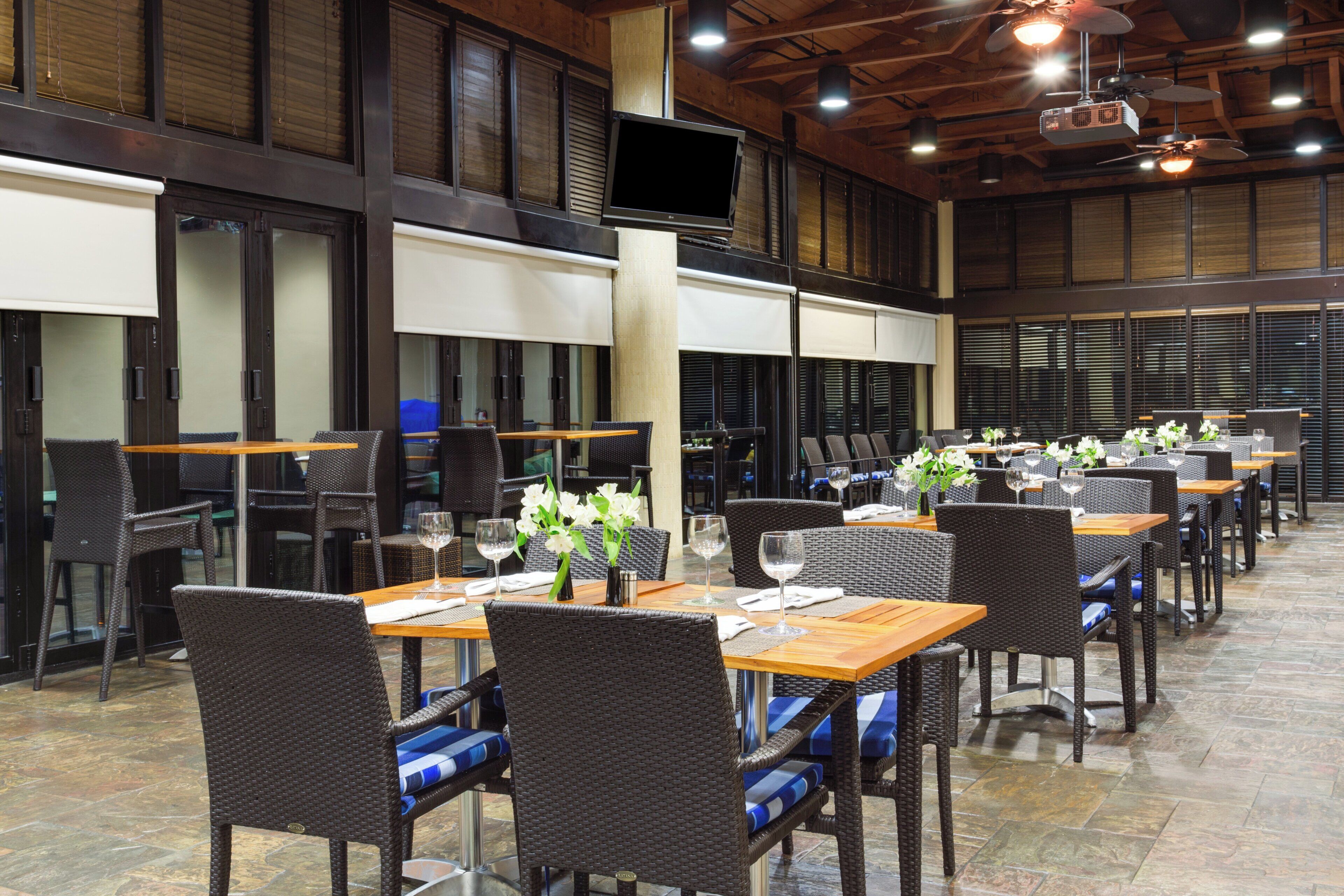 A restaurant with multiple tables and chairs, a television mounted on the wall, and a ceiling fan.