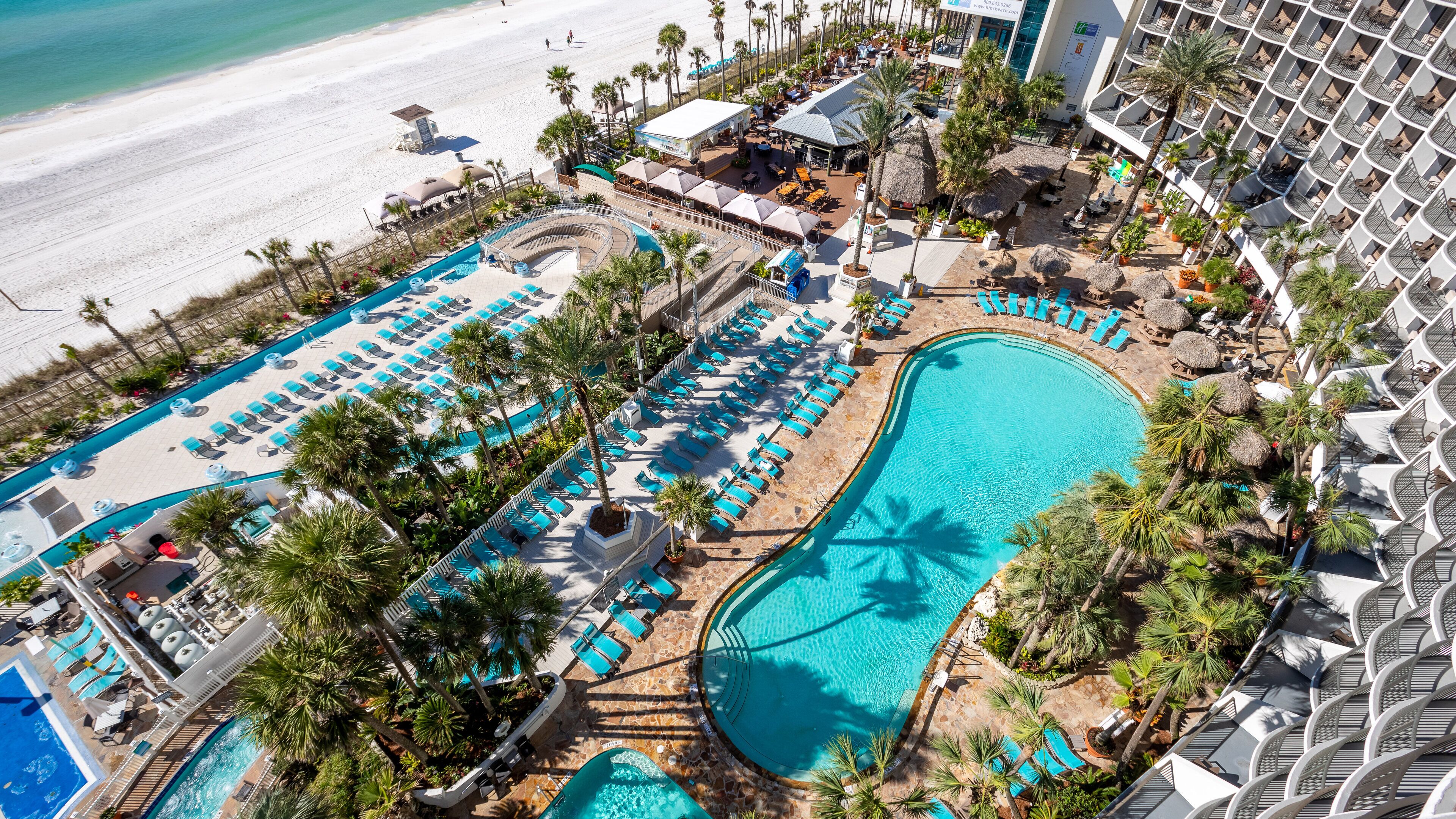 Un resort con una amplia zona de piscina, múltiples tumbonas y vista a la playa.