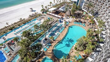 A resort with a large pool area, multiple lounge chairs, and a beach view.