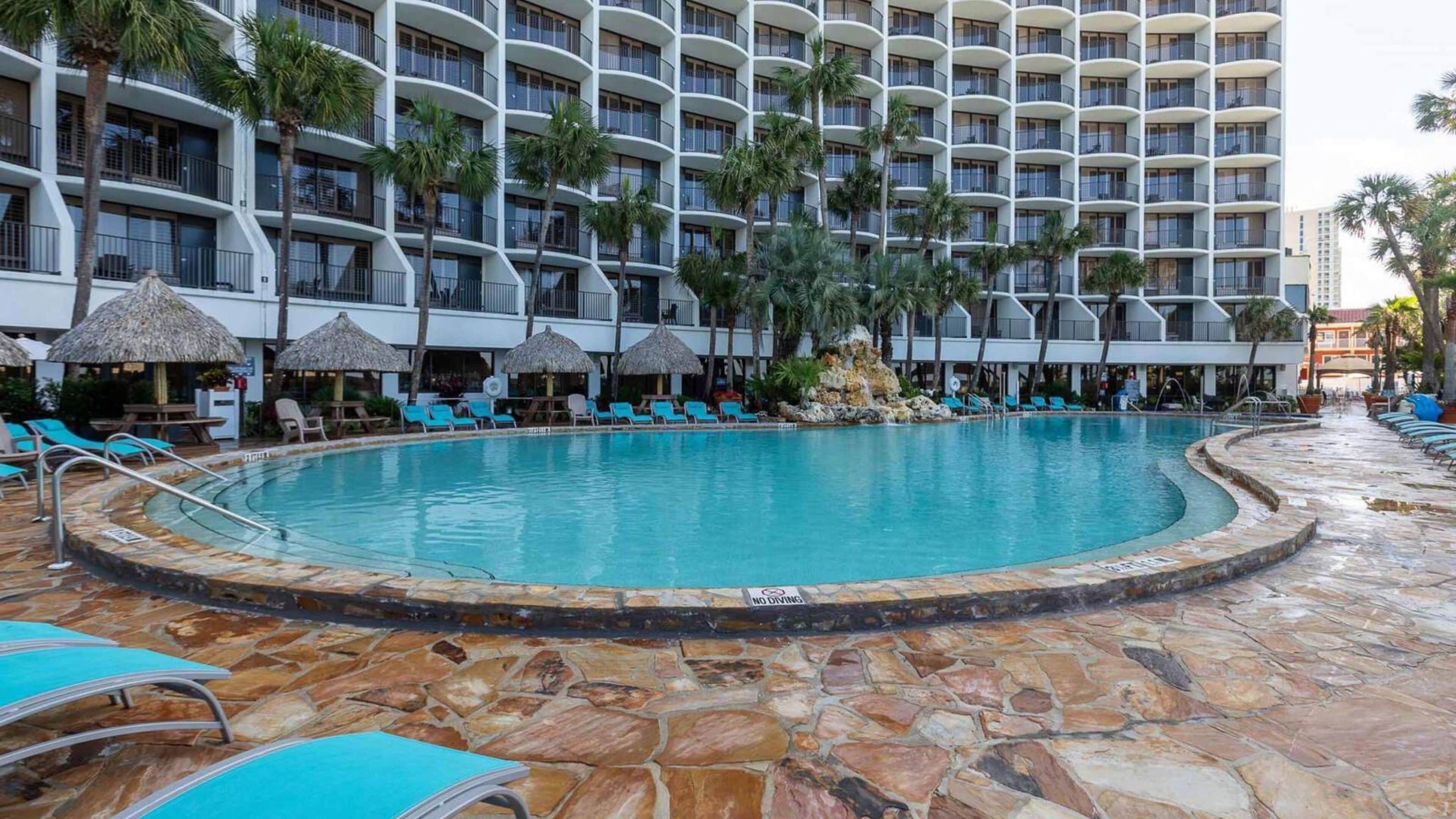 Ein Hotelpoolbereich mit rundem Pool, Liegestühlen und Palmen.
