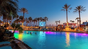 A pool area with palm trees, a large screen, and lounge chairs. - Holiday Inn Resort Panama City Beach by IHG (Panama City Beach)