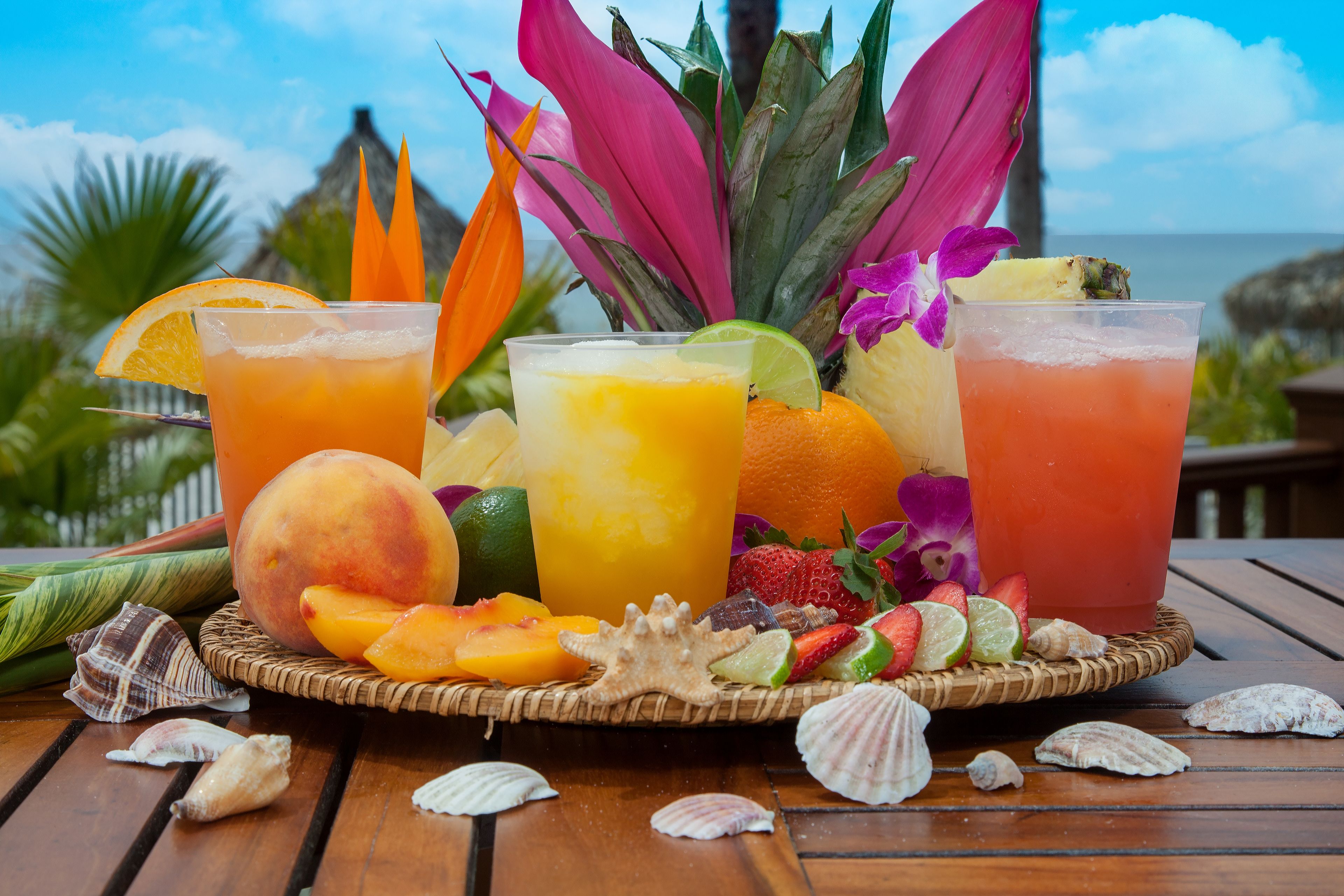 Preparación de una bebida tropical con frutas variadas y una vista a la playa al fondo.