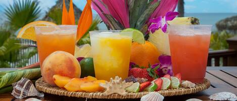 Preparación de una bebida tropical con frutas variadas y una vista a la playa al fondo.