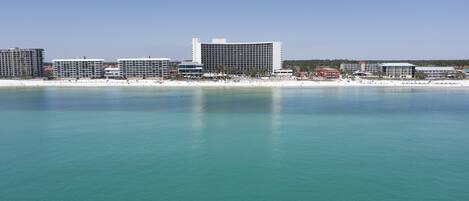 A coastal cityscape with a prominent hotel featuring a modern design, situated near a beach with clear turquoise waters.